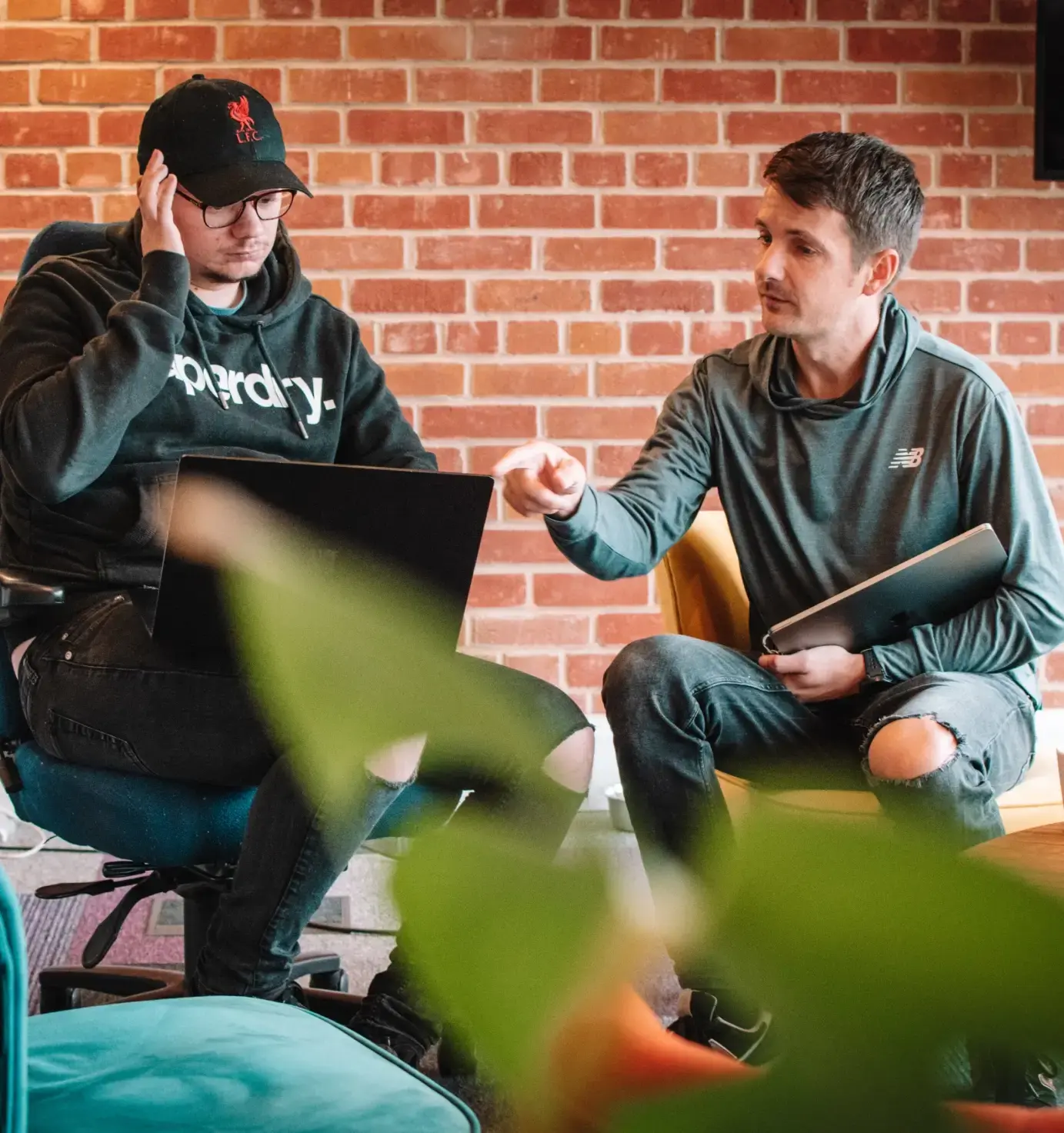 two people sat together looking at a laptop and discussing one of them is gesturing and pointing at the screen