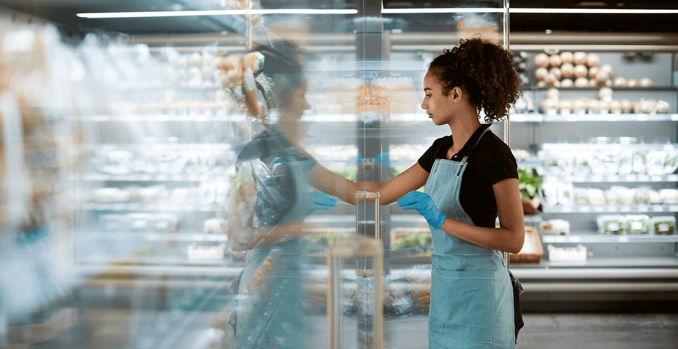 Woman with gloves and an apron on putting items into a refrigeration unit.